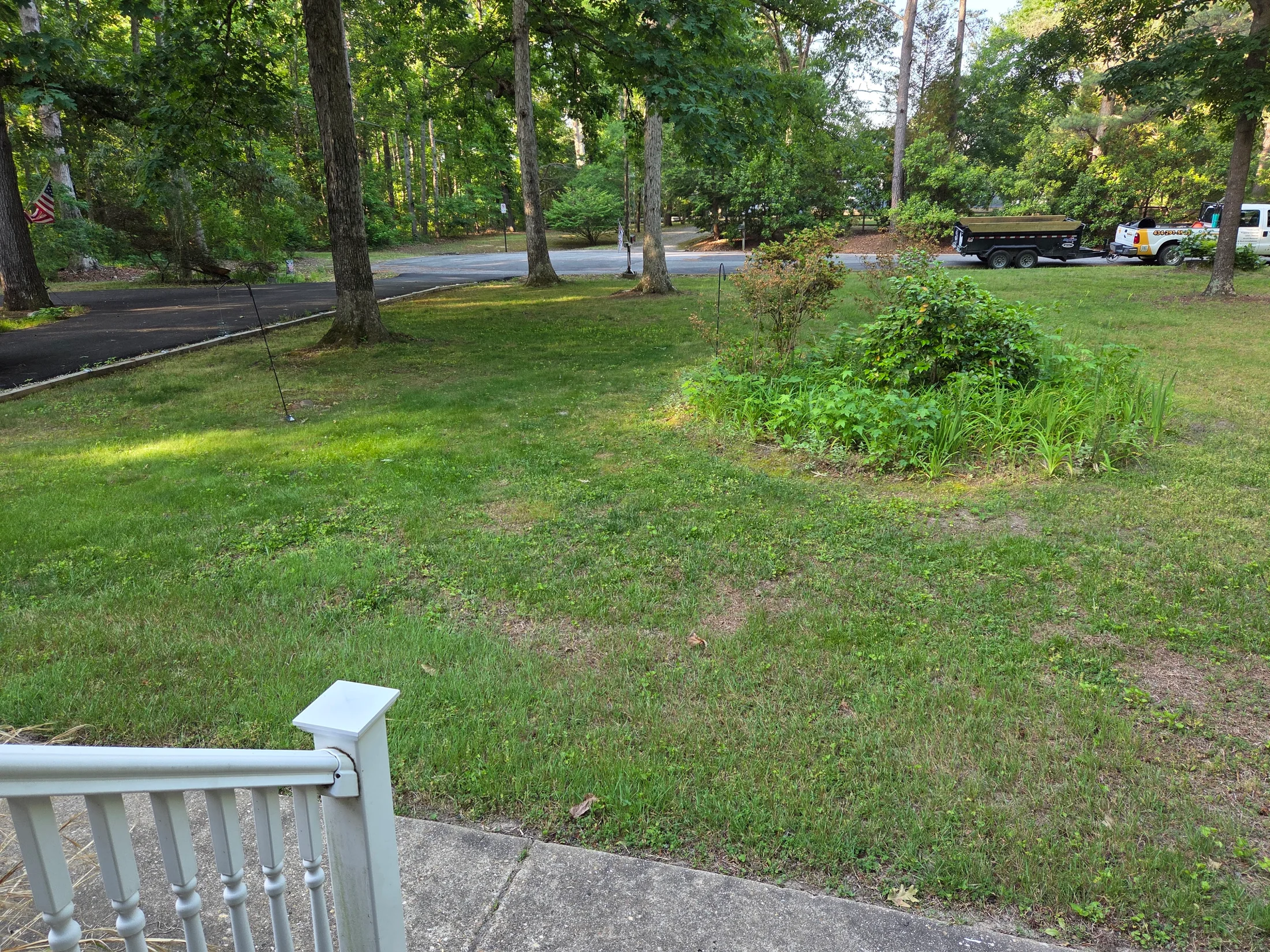 Open residential yard bordered by woods with Sunny Landscaping equipment at the property edge