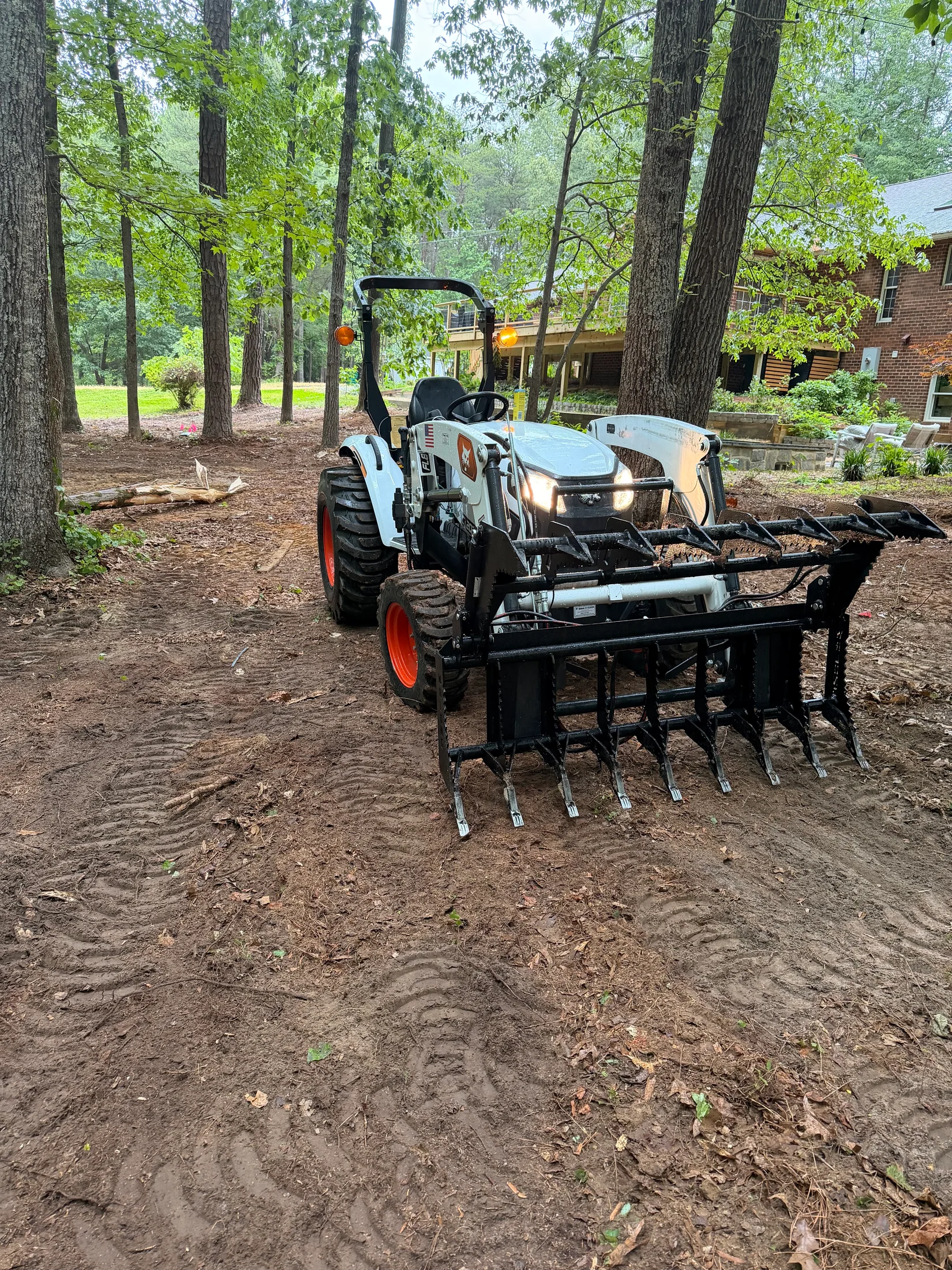 Compact loader working on exposed ground in a wooded residential yard