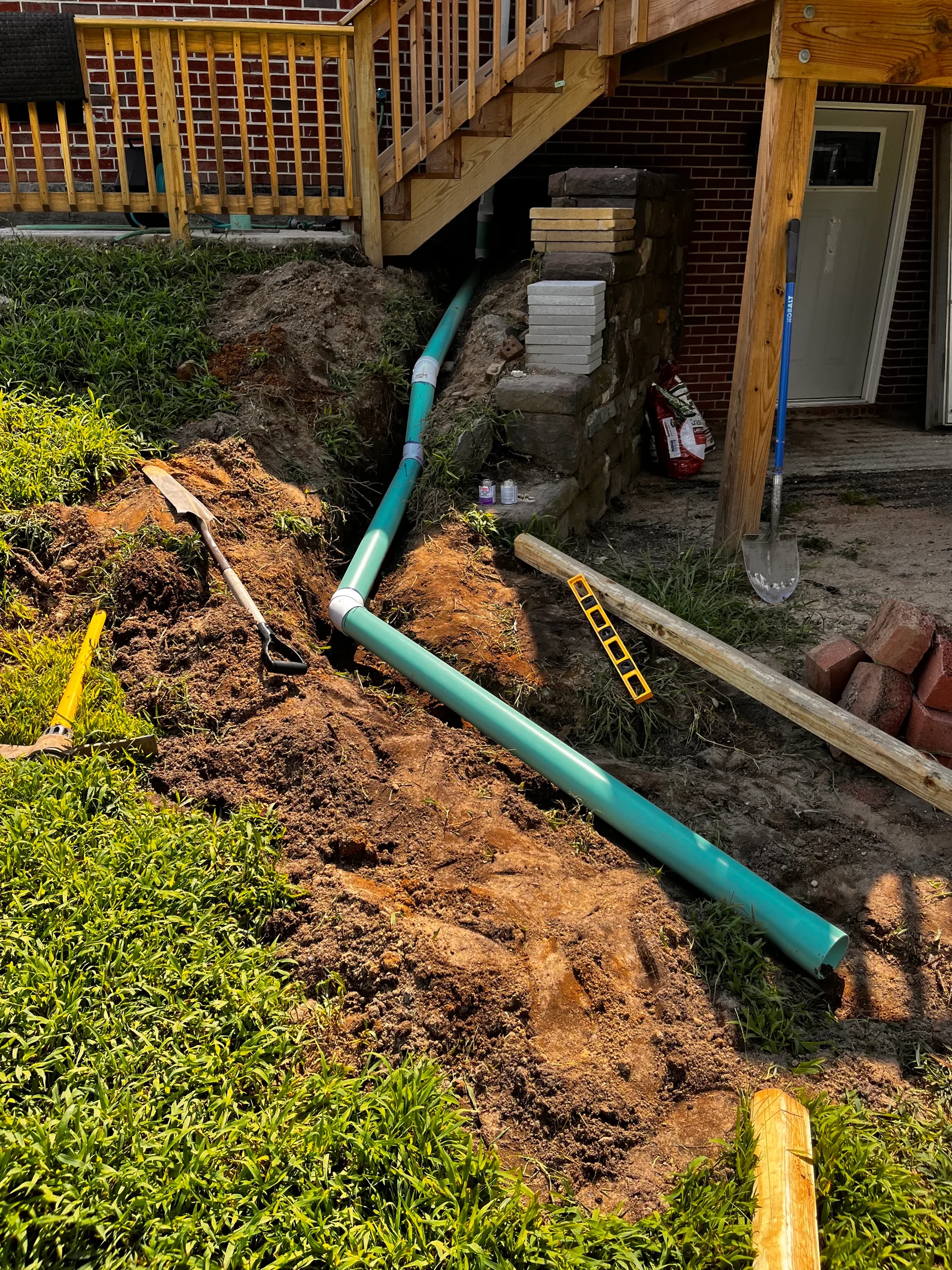 Green drainage pipe laid through an open trench beside a backyard deck