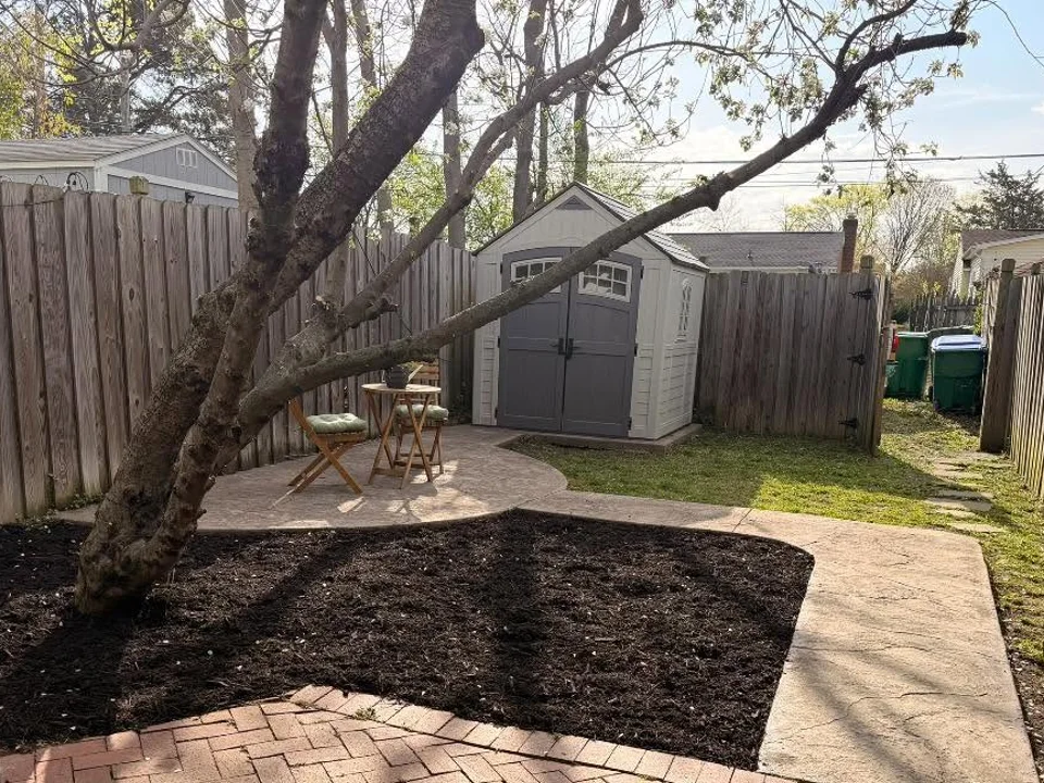 Dark mulch around a mature tree between existing brick paving and a concrete path