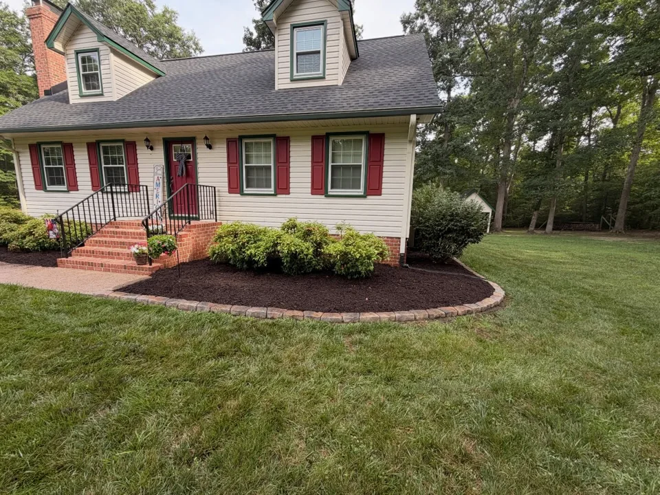 Curved stone-edged mulch beds and shrubs across the front of a home