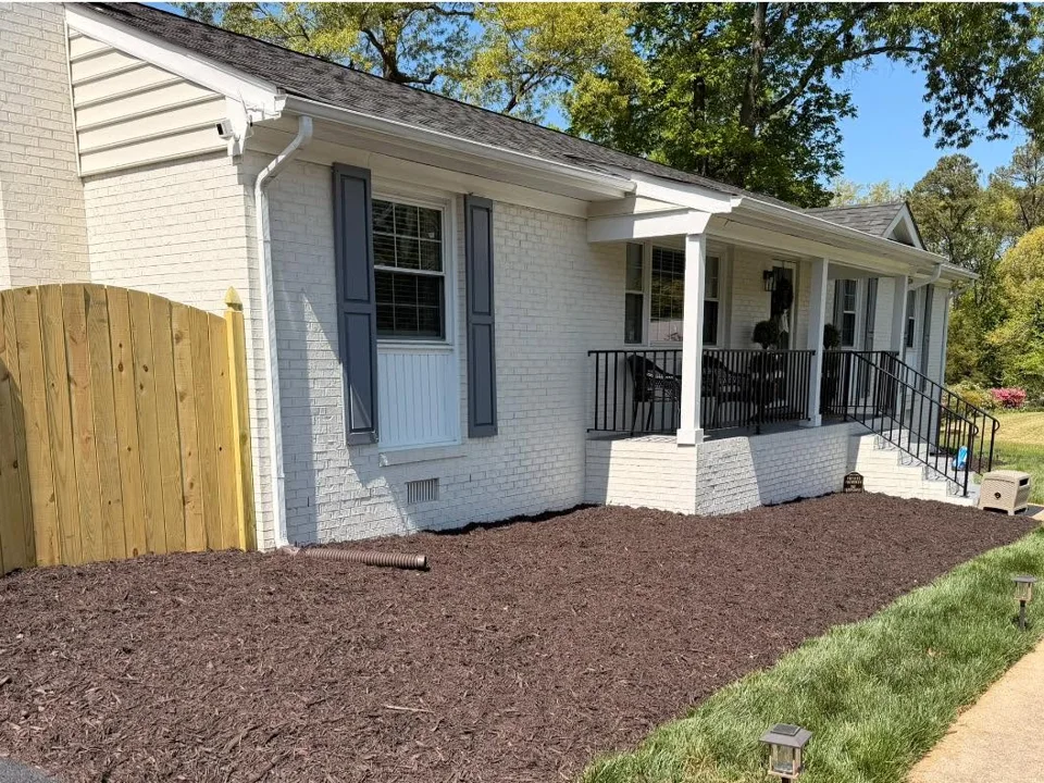 Broad newly mulched bed beside a white porch and concrete walkway