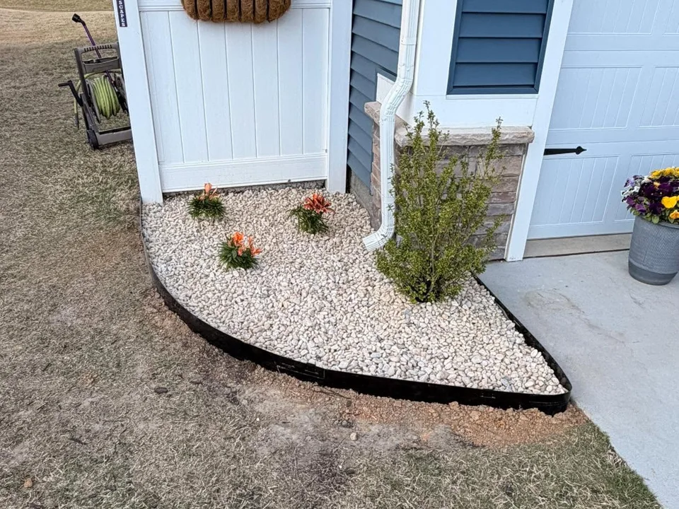 Curving white-stone planting bed beside blue siding and a white gate